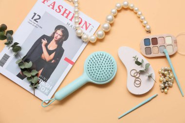 Mücevherli dergi, göz falı paleti, turuncu arka planda saç ve makyaj fırçası.