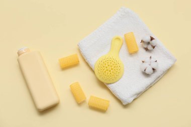 Saç fırçası, bigudiler, bir şişe şampuan ve sarı arka planda pamuk çiçekli havlular.