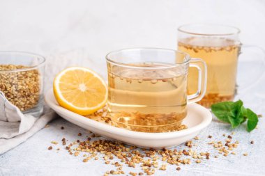 Açık arkaplanda bir bardak taze karabuğday çayı, nane ve limon.