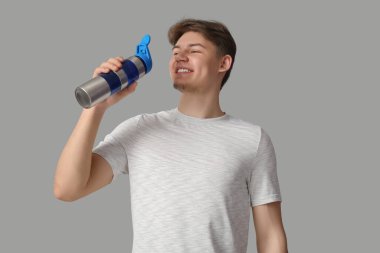 Gri arka planda su içen genç bir sporcu.