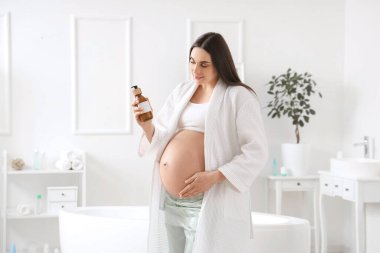 Banyoda bir şişe kremalı hamile kadın.