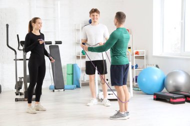 Erkek antrenör ve spor salonunda ip atlama egzersizi yapan gençler.