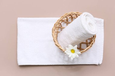 Temiz yumuşak havlular, hasır sepet ve kahverengi arka planda papatya çiçeği olan kompozisyon