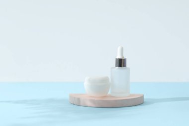 Mavi arka planda alçı standı, bir kavanoz krema ve bir şişe serum.