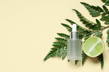 Limonun yarısı, eğreltiotu dalı ve sarı arka planda bir şişe kozmetik ürünü olan kompozisyon, yakın plan.