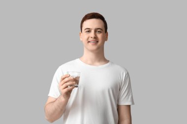 Gri arka planda bir bardak temiz suyu olan yakışıklı bir genç.
