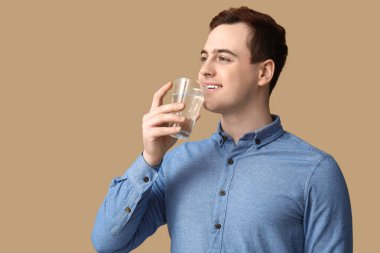 Handsome young man drinking clean water on brown background