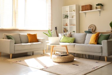 Gri kanepeleri, çiçekleri, sehpası ve raf ünitesi olan güzel bir oturma odası.