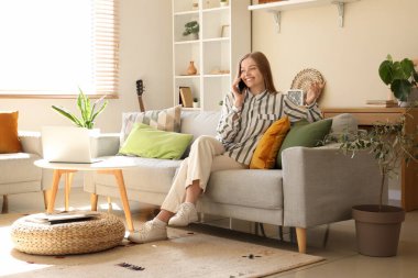 Kanepede oturan ve oturma odasında cep telefonuyla konuşan genç bir kadın.