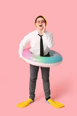 Şişme yüzüklü ve paletli bir ofis çalışanı pembe arka planda tatil hayali kuruyor.