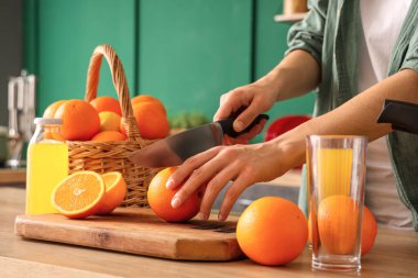 Yeşil mutfakta turuncu sepetin yanında turuncu kesen genç bir kadın.