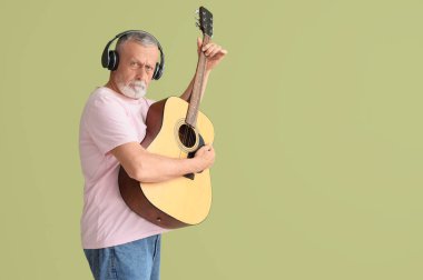 Kulaklıklı, yeşil arka planda gitar çalan olgun bir adam.