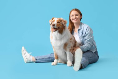 Avustralya çoban köpeği olan genç bir kadın mavi arka planda oturuyor.