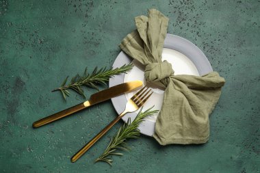 Yeşil grunge arka planda peçete, çatal bıçak ve biberiye ile şık masa ayarları