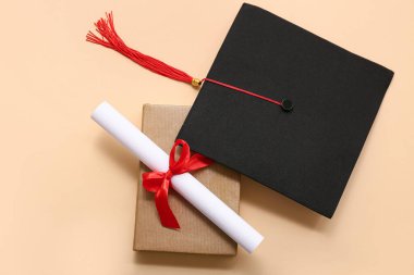 Kırmızı kurdeleli diploma, bej arka planda kitap ve mezuniyet şapkası.