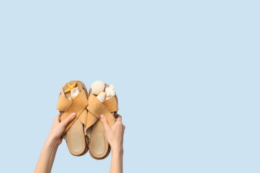 Mavi arka planda deniz yıldızı ve kabuk dolu parmak arası terlikler tutan eller.