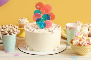 Sarı duvara karşı doğum günü partisi için pasta ve şekerli bir masa.