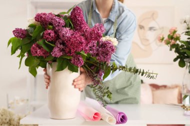 Çiçek stüdyosunda vazo dolusu leylağı olan bir çiçekçi.