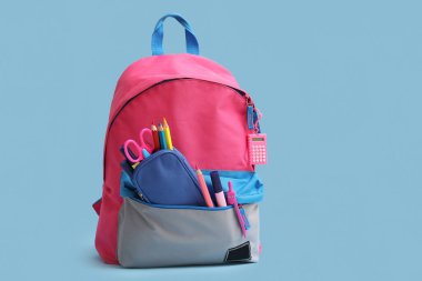 Mavi arka planda kırtasiye malzemesi olan pembe okul çantası