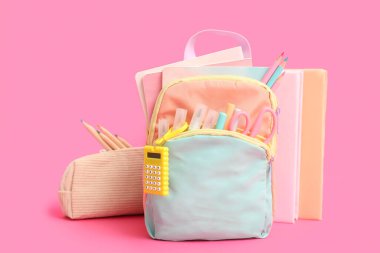 Kırtasiyeli mavi okul çantası ve pembe arka planlı kitaplar.