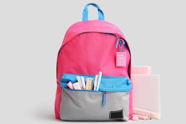 Kırtasiyeli pembe okul çantası ve gri arkaplan üzerine not defterleri.