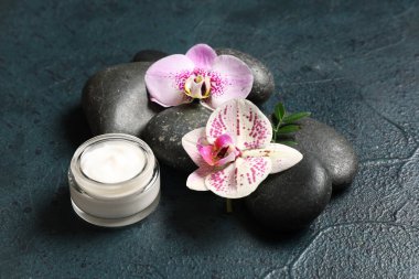 Koyu arkaplanda spa taşları, krema ve orkide çiçekleri