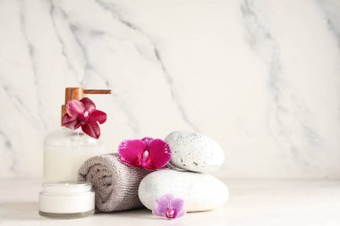 Spa taşları, krem, losyon, havlu ve orkide çiçekleri açık arkaplanda
