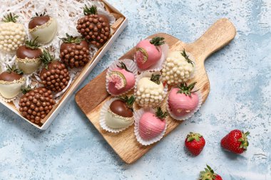 Açık mavi arka planda çikolata kaplı çilekli kutu ve ahşap tahta