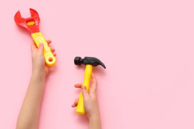 Pembe arka planda oyuncak inşaat aletleri olan çocuk elleri, yakın plan