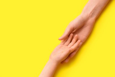 Kadın ve çocukların elleri sarı arkaplanda, yakın plan.