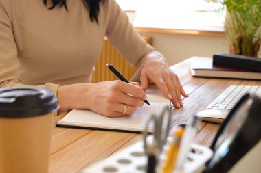 İş yerindeki not defterine bir fincan kahve ve klavyeyle şık bir ofiste yazan genç bir kadın.