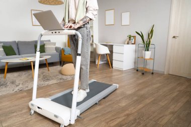 Evde koşu bandında dizüstü bilgisayarla çalışan yakışıklı bir iş adamı.