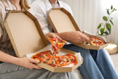 Karton kutularda lezzetli pizzalar taşıyan genç bir çift yatak odasında oturuyor, yakın plan.