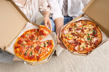 Karton kutularda lezzetli pizzalar tutan ve evdeki halıya oturan genç çift, yakın plan.