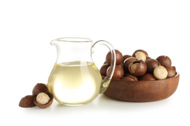 Beyaz arka planda bir sürahi macadamia yağı ve fındık.