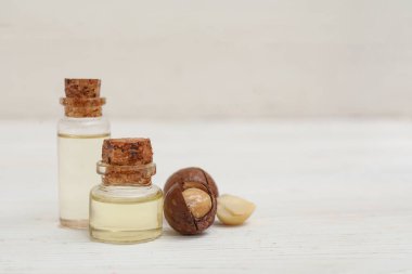 Makadamia yağı şişeleri ve hafif ahşap arka planda fındıklar.