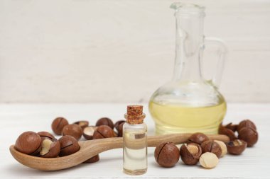 Bir sürahi macadamia yağı ve açık ahşap masada fındık.