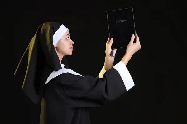 stock image Young nun with Bible on black background