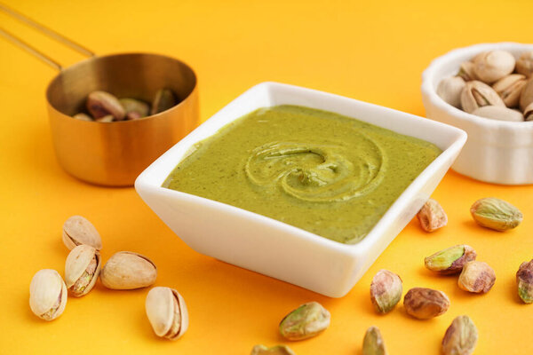 Вкусная фисташковая паста в миске и измерительная чашка на желтом фоне