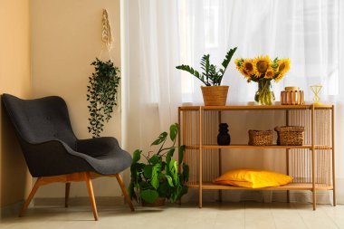 Güzel ayçiçekleri olan vazolar ve odandaki koltuğun yanındaki raflarda saksı bitkisi.