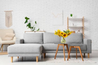 Oturma odasındaki sehpada ayçiçekli rahat bir kanepe ve vazo.