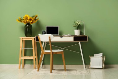 Taburede ayçiçekli vazo ve çalışma odası yeşil duvarın yanında.