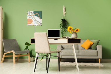 Çalışma odası ve vazo, yeşil duvarın yanında ayçiçekleri var.