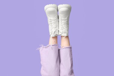 Leylak arkaplanlı beyaz deri çizmeli genç kadın bacakları.