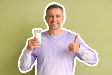 Yeşil arka planda baş parmağını gösteren bir bardak sütle olgun bir adam.