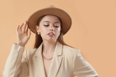 Şık ceketli ve bej arka planda şapkalı, şık bir genç kadın.