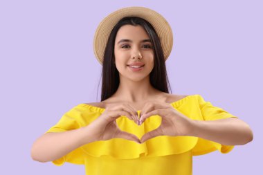 Elleri leylak arkaplanda kalp yapan genç bir kadın.