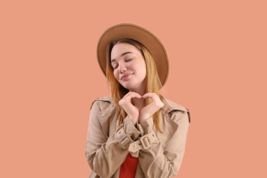 Elleri pembe arka planda kalp yapan genç bir kadın.