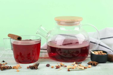 Çaydanlık ve bir bardak sıcak meyve çayı yeşil ahşap masada.