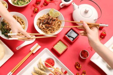 Çubuklu kadın elleri ve kırmızı arka planda farklı Çin yemekleri.